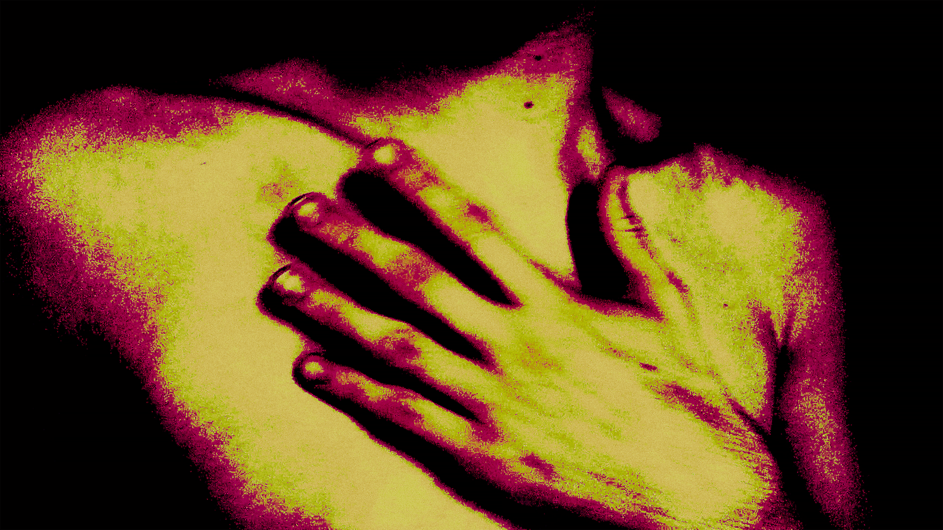 A still from the experimental short film, Terror, with a close-up of a person's chest with their hand lying over their heart. The colours are distorted to only bright pink, yellow and black, and a pixelated effect is present.
