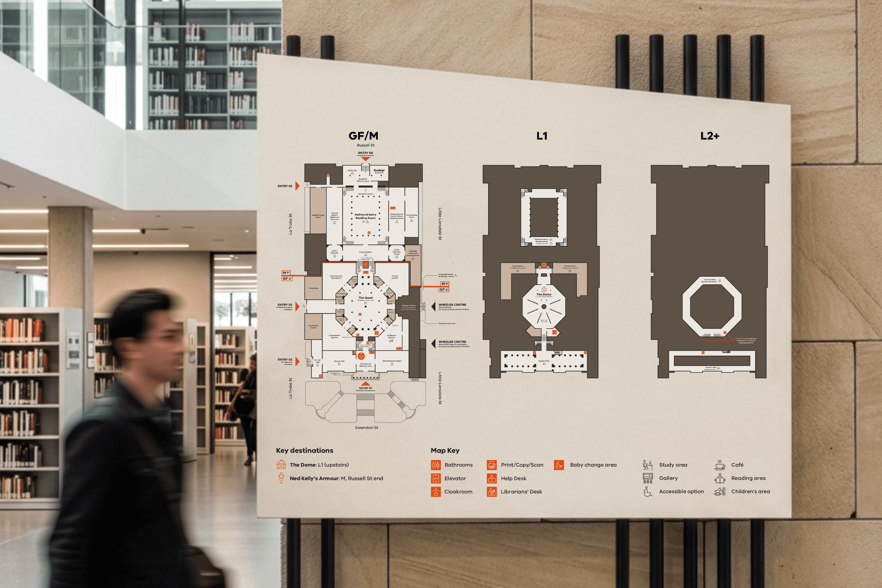 A diagrammatic map of the State Library Victoria's complex interior on a physical sign in a library. A blurred man is about to walk in front.